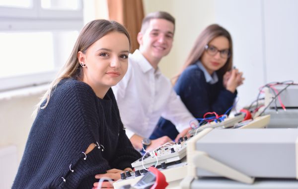Group of young students in technical vocational training with teacher, the lesson in technical college, with young female student in front of camera.