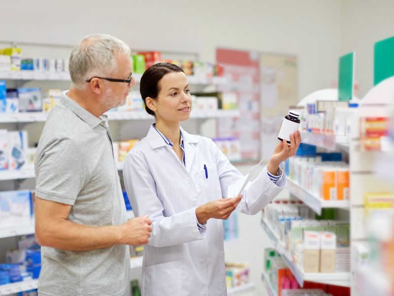 medicine, pharmaceutics, health care and people concept - happy pharmacist and senior man customer with drug and prescription at drugstore